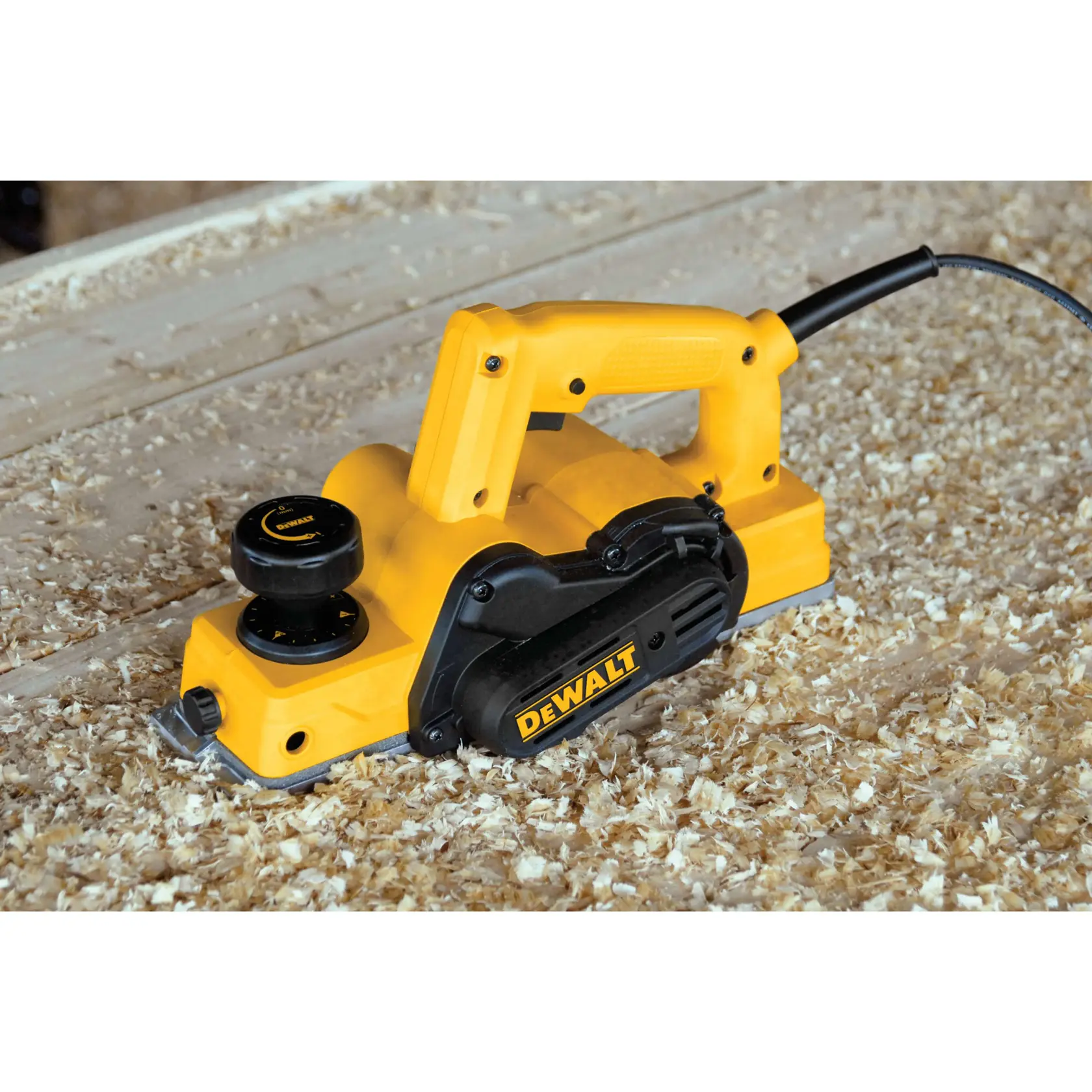 Un cepillo eléctrico de mano amarillo y negro DEWALT se muestra en uso sobre una superficie de trabajo de madera, rodeado de virutas de madera.