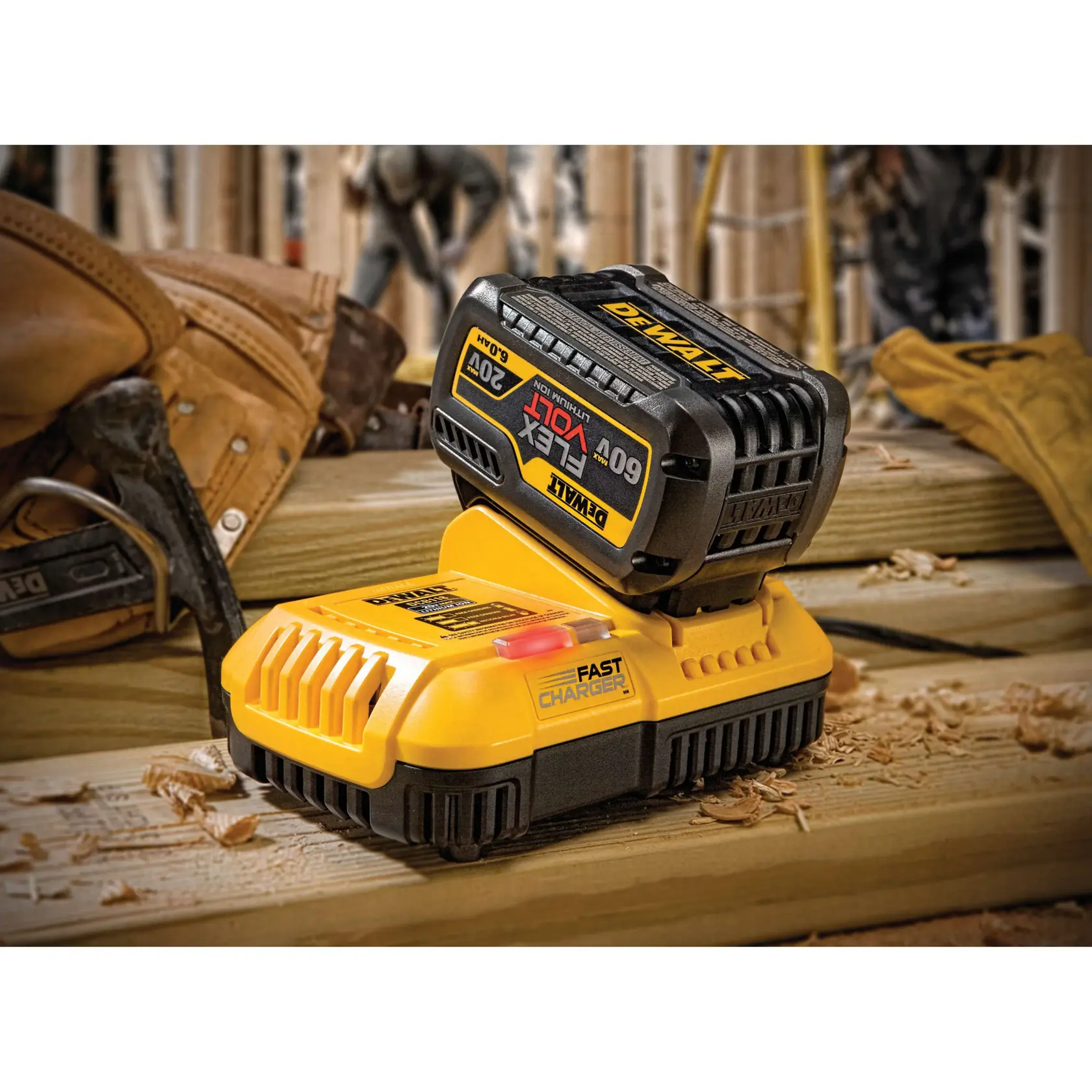 Una batería DEWALT 60V/20V MAX FLEXVOLT de ion de litio sobre un cargador rápido DEWALT, situada sobre una viga de madera en una obra. Guantes de trabajo y herramientas son visibles al fondo.