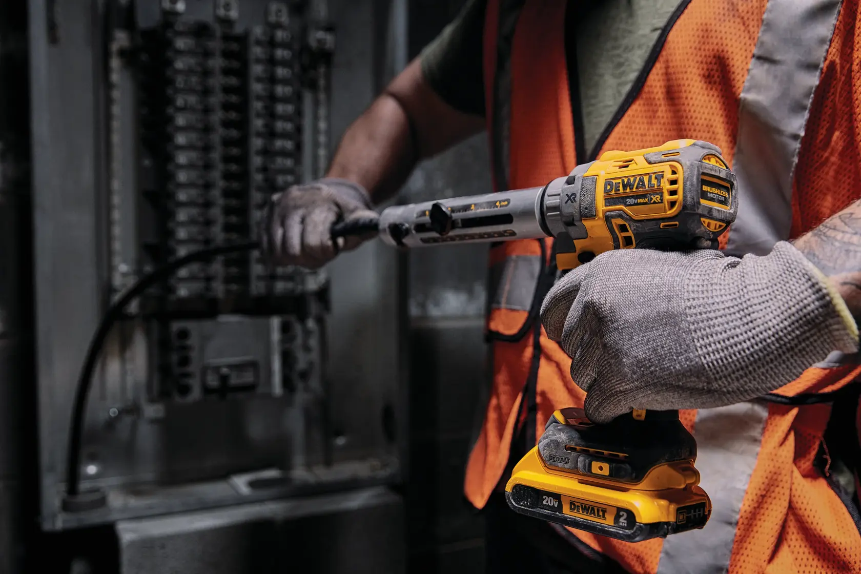 Trabajador usa herramienta DEWALT 20V cerca de un panel eléctrico, con guantes y chaleco de seguridad naranja.