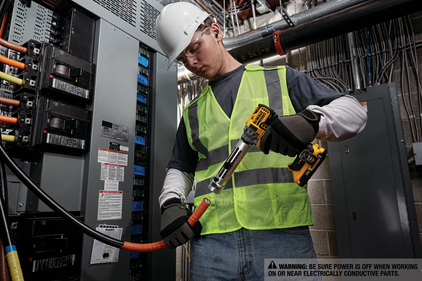 Un trabajador con casco blanco, guantes de seguridad y chaleco reflectante verde neón utiliza una herramienta inalámbrica DEWALT para cortar un cable eléctrico en un entorno industrial. El trabajador está junto a un panel eléctrico con varios cables y disyuntores. Se ve una etiqueta de advertencia que recomienda asegurarse de que la corriente está apagada al trabajar cerca de partes conductoras eléctricas.