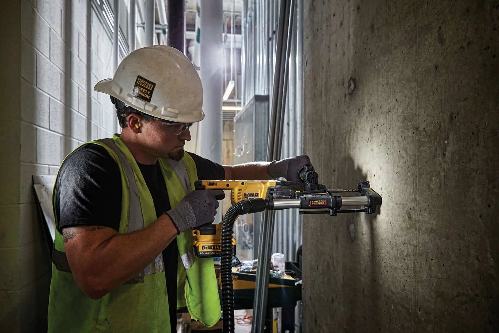 Una persona con casco de seguridad, guantes y chaleco reflectante usa un taladro rotativo amarillo DEWALT (SKU: DCH133B) para perforar una pared de concreto en un sitio de construcción. El taladro está conectado a un sistema de extracción de polvo para una operación más limpia. El rostro de la persona está desenfocado.