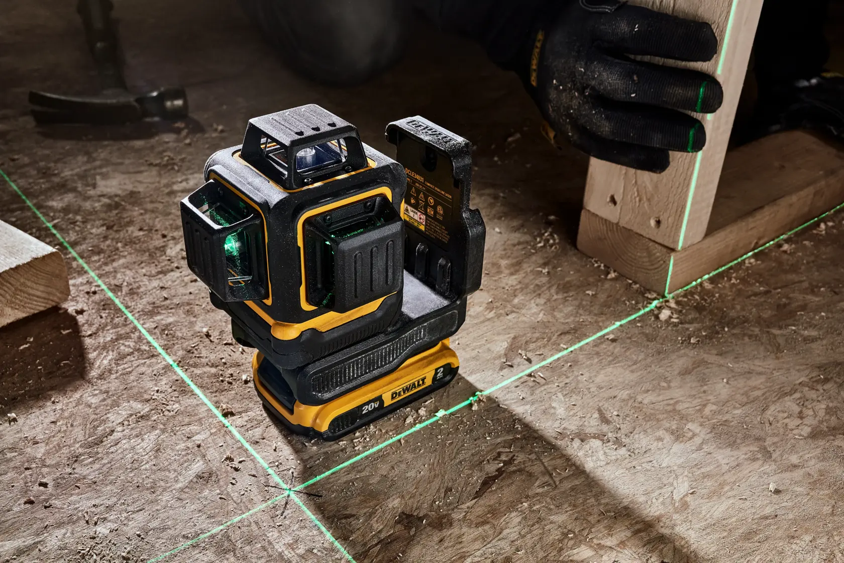 Una herramienta de nivel láser DEWALT 20V proyecta líneas láser verdes brillantes sobre un piso de madera. Una persona con guantes negros está alineando una pieza de madera utilizando las líneas láser.