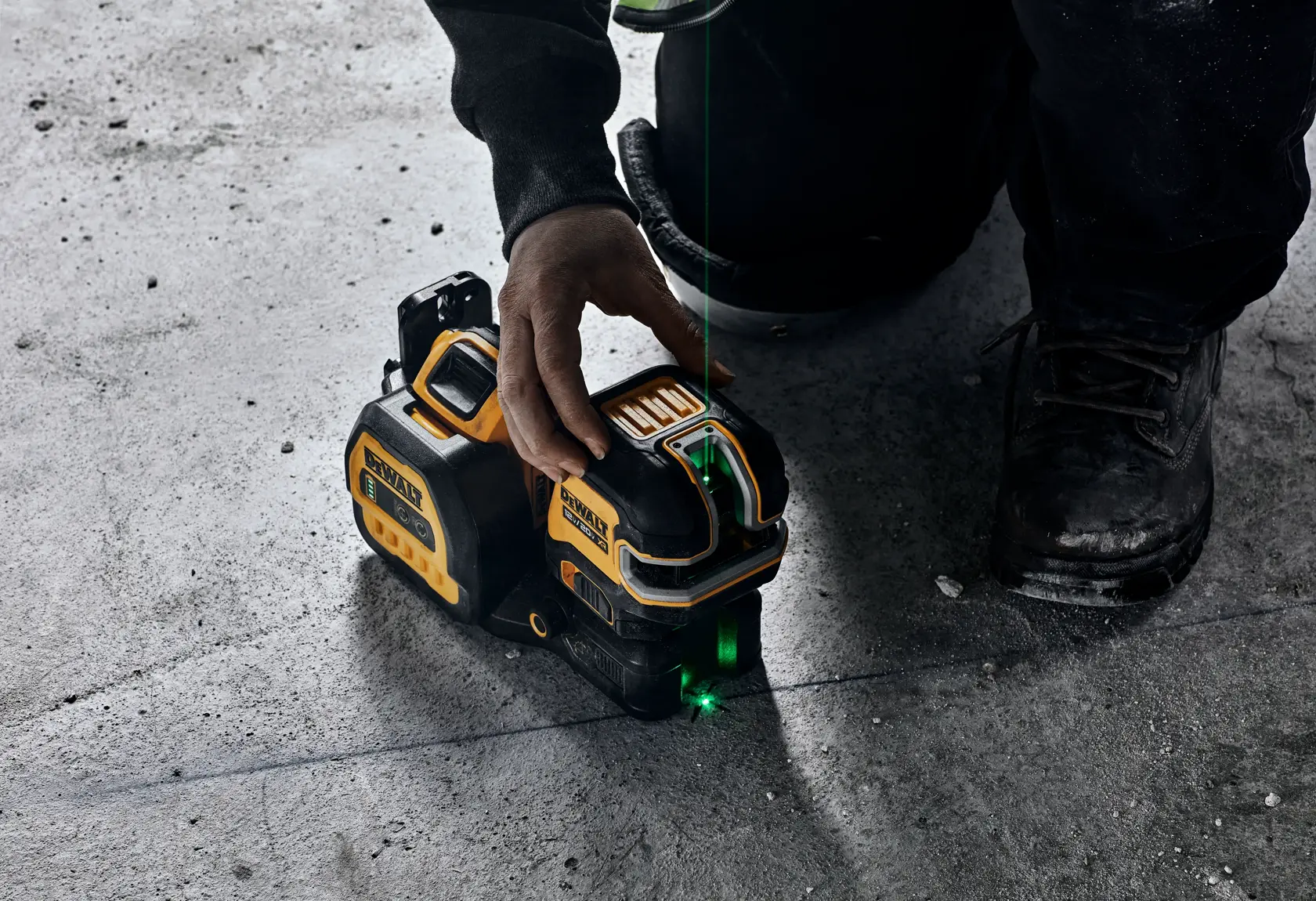 Una persona utiliza una herramienta de nivel láser DEWALT sobre un suelo de concreto. El dispositivo emite una línea láser verde para nivelar y alinear con precisión.
