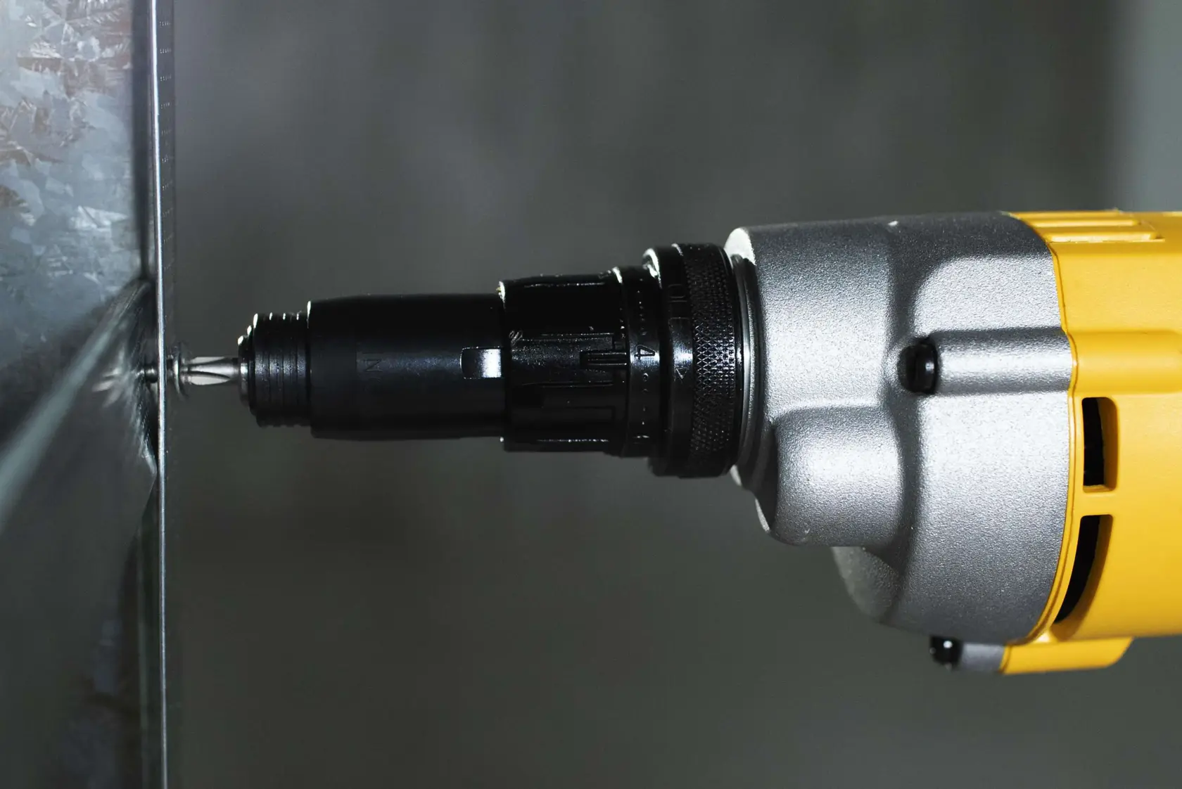 Vista en primer plano de un destornillador eléctrico DEWALT DW268 usado para atornillar un tornillo en una superficie metálica.
