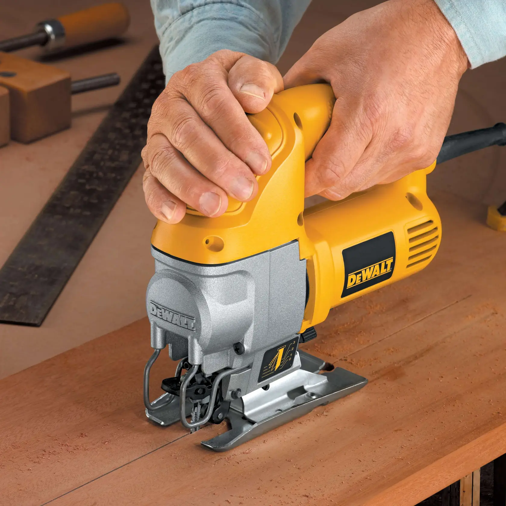 Una persona usa una sierra de calar amarilla DEWALT para cortar una pieza de madera sobre un banco de trabajo.