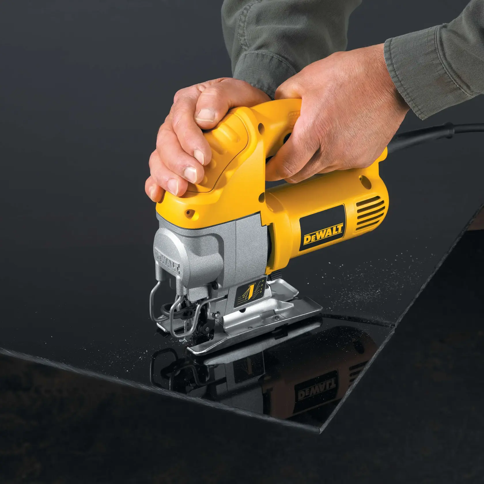 Una persona utiliza una sierra de calar amarilla DEWALT para cortar una hoja de material negro. Las manos guían la herramienta a lo largo de la línea de corte.