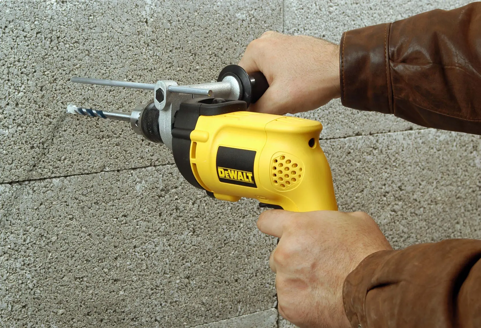 Una persona utiliza un taladro eléctrico amarillo DEWALT para perforar una pared de concreto.