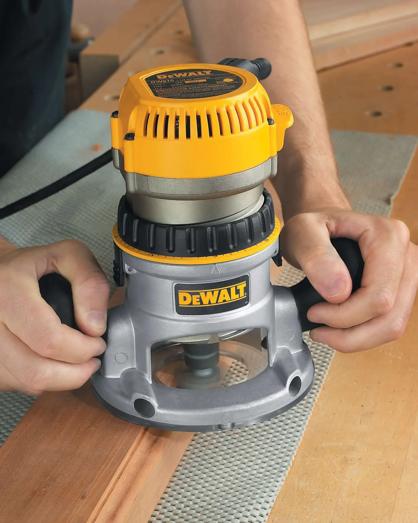Vista de cerca de una persona usando una fresadora de madera DEWALT DW616 sobre una pieza de madera en un taller.