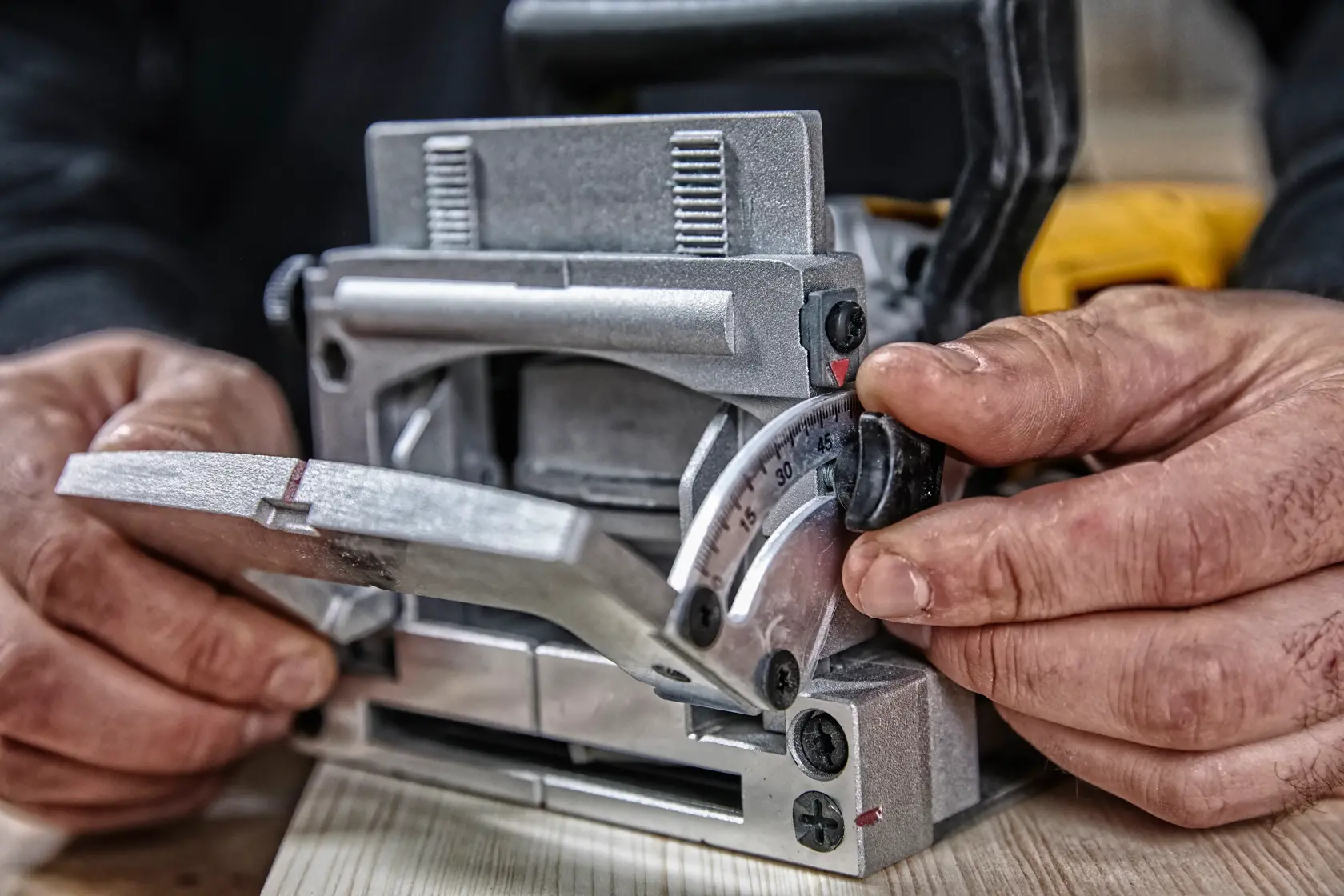 Primer plano de manos ajustando la configuración de ángulo en una herramienta de ensamblaje DEWALT para trabajos en madera, con la herramienta apoyada sobre una tabla de madera.