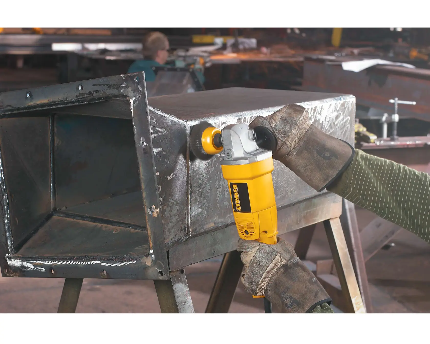 Una persona con guantes protectores utiliza una amoladora angular amarilla DEWALT (modelo DW831) para pulir el borde de una caja metálica en un taller.