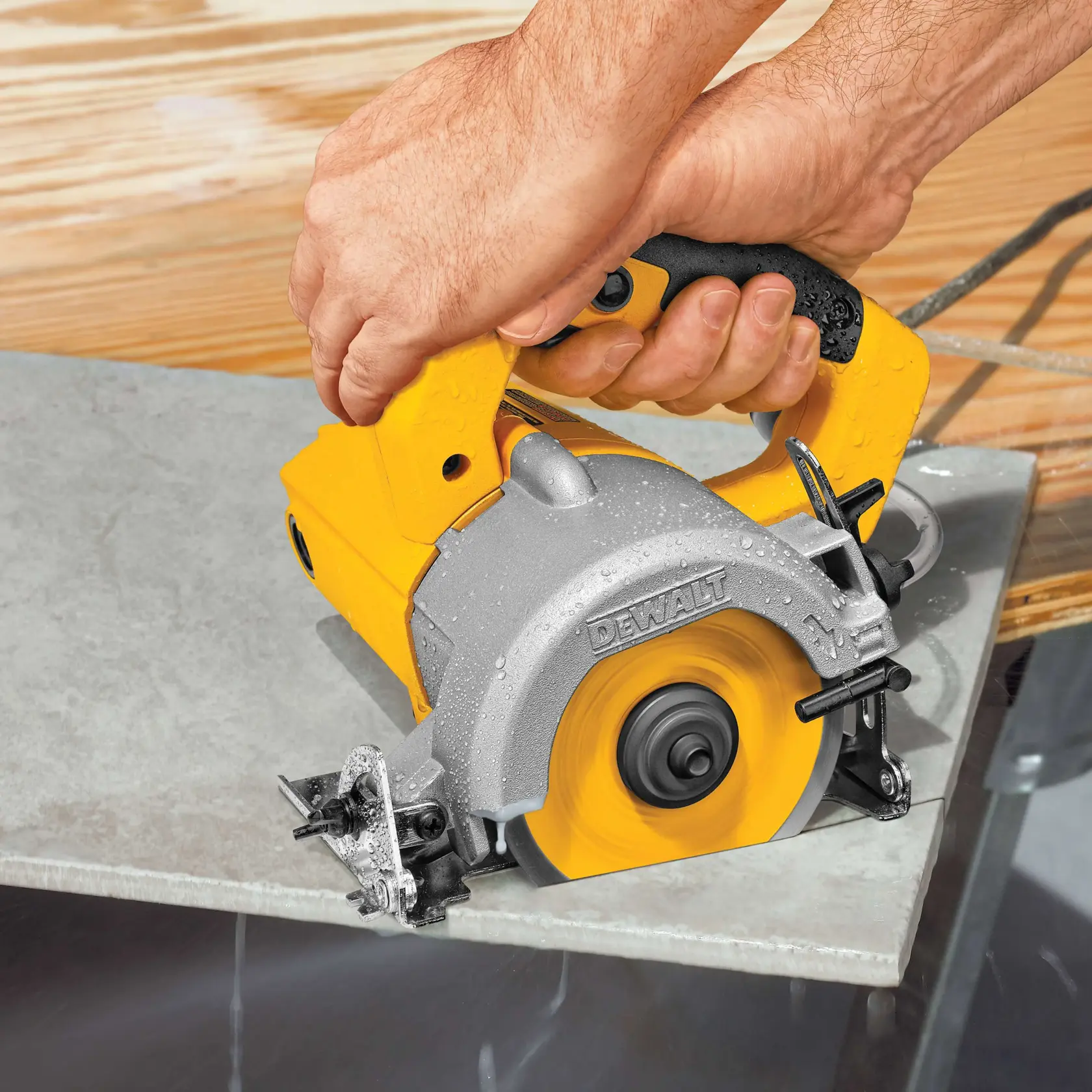 Primer plano de una persona utilizando una sierra para azulejos manual DEWALT para cortar una pieza de azulejo. La sierra es amarilla y plateada, y se utiliza agua para enfriar la hoja durante el corte.