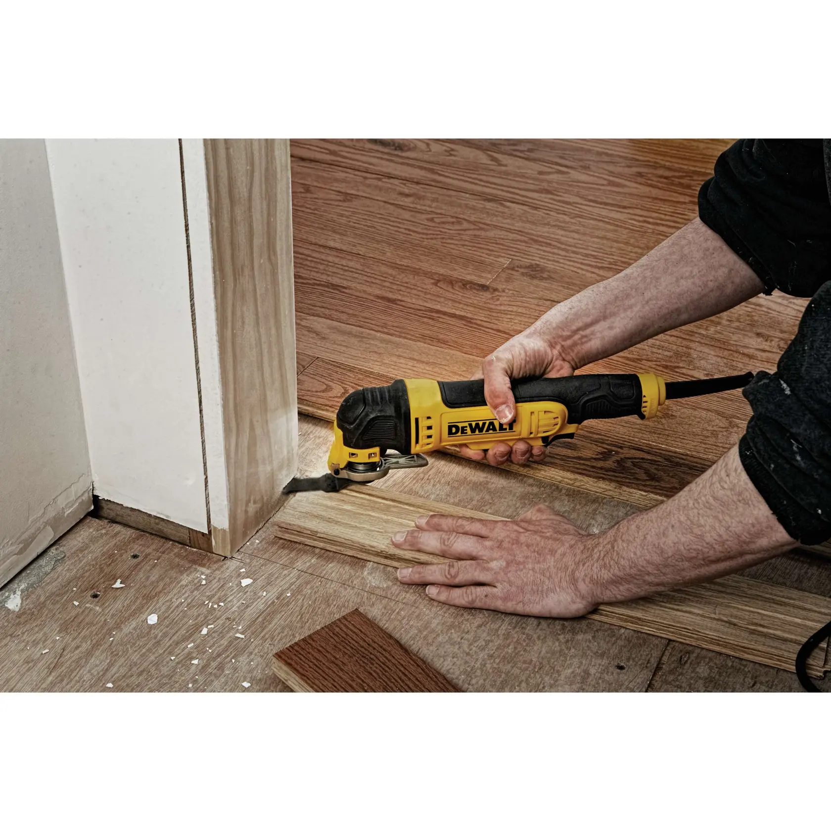 Una persona utiliza una multiherramienta oscilante amarilla y negra DEWALT para cortar el suelo de madera cerca de una puerta.