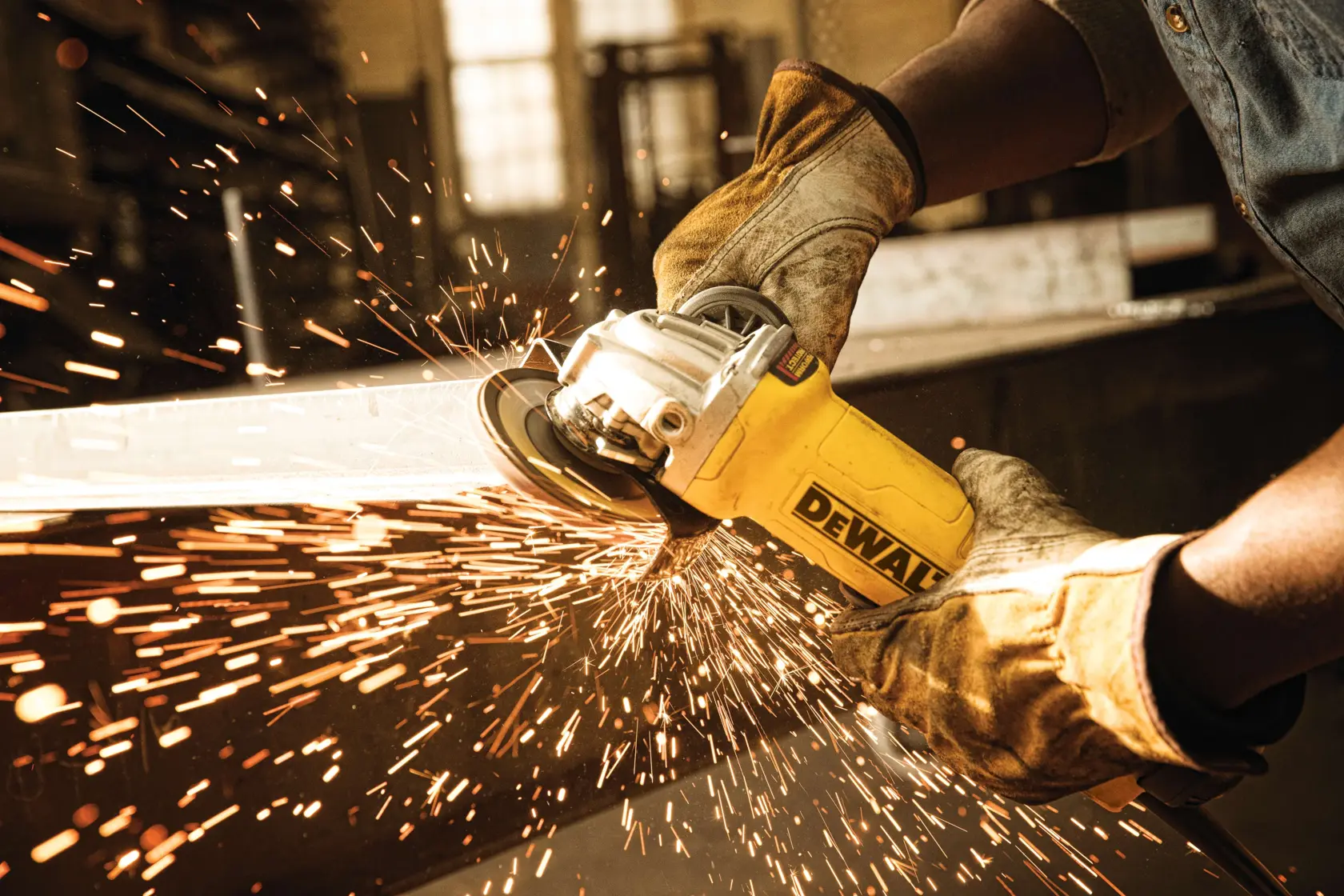 Una persona con guantes protectores usa una amoladora angular amarilla DEWALT para cortar o pulir metal, produciendo chispas brillantes en un taller.