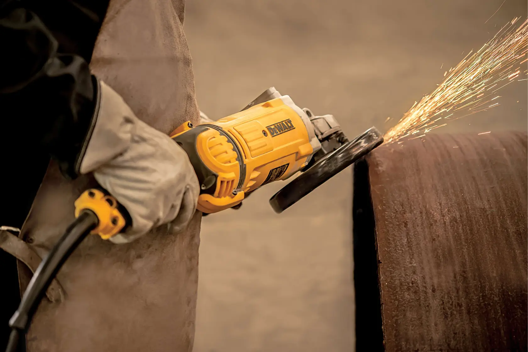 Una persona con guantes protectores utiliza una amoladora angular DEWALT para pulir una tubería metálica grande, produciendo chispas.