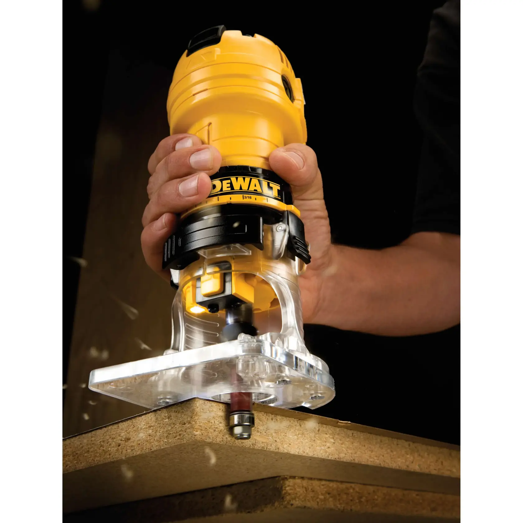 Imagen en primer plano de una fresadora compacta DEWALT DWE6000 utilizada para recortar el borde de una tabla de madera, sostenida por la mano de una persona.