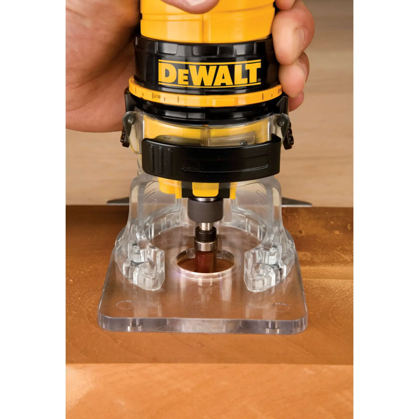 Imagen en primer plano de una persona usando una fresadora manual DEWALT con una base transparente para recortar o dar forma al borde de una pieza de madera.